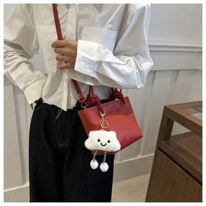 Detail of red pebbled leather bucket bag with cute cloud plush charm and shoulder strap