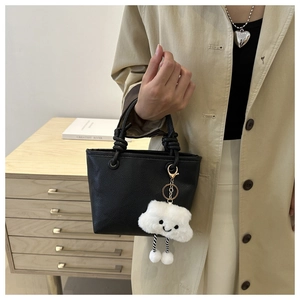 Detail of black lychee leather bucket bag with woven handle and plush cloud charm decor