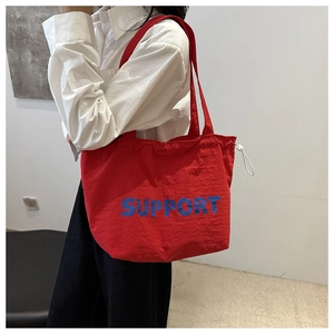 Detail of red tote bag featuring blue SUPPORT lettering and white side drawstring buckle