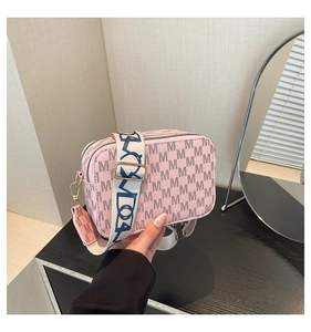 Detail of pink monogram crossbody bag with pink leather tag and gold-tone zippers