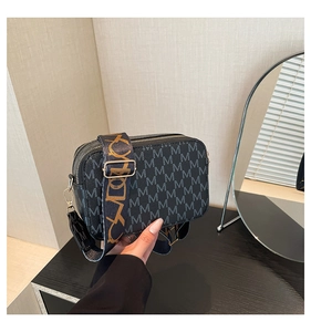 Detail of black crossbody bag with double zippers and golden pattern jacquard strap