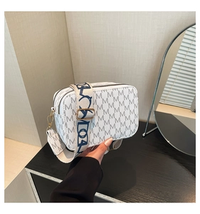 Close-up of white crossbody bag with M logo print, wide fabric strap and gold hardware
