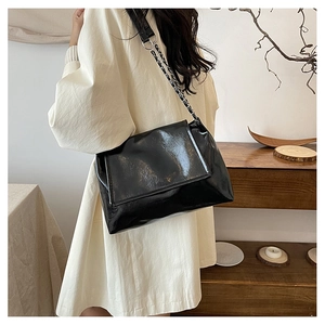 Détail du sac à bandoulière noir brillant avec chaîne argentée porté par un mannequin