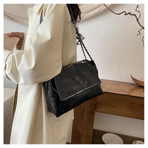 Détail d'un sac bandoulière noir brillant avec chaîne sur un trench-coat beige chic