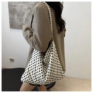 Polka dot oversized knit tote bag shown worn on shoulder in a minimalist indoor setting