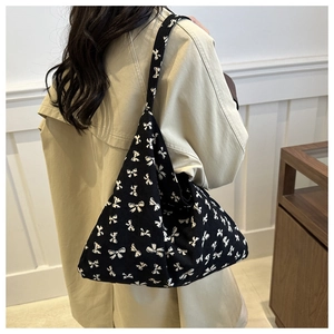 Lifestyle view of a large black knit tote bag with white bow print worn with a beige coat
