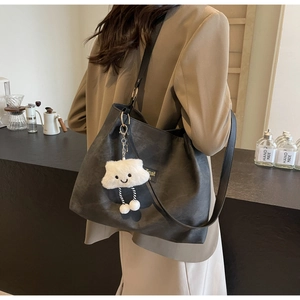 Detail of a black matte tote bag with a white plush cloud charm on a shoulder strap
