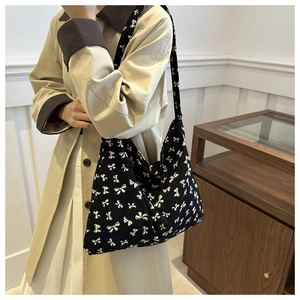 Detailed view of black tote bag with white bow pattern worn by a model in a minimal room