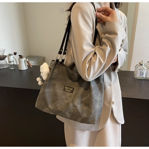 Detail of dark grey vintage tote bag with black logo patch and plush charm accessory