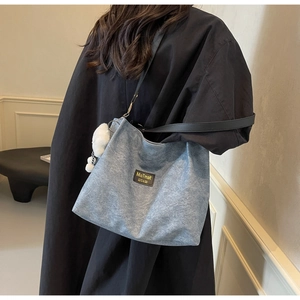 Close-up of blue denim tote bag featuring black leather logo patch and white plush charm