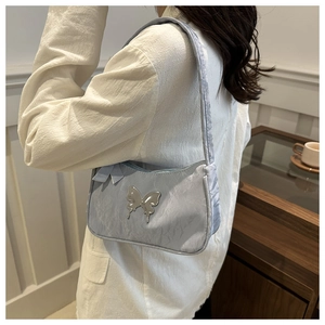Detail of light blue pleated underarm bag with silver butterfly charm on a model shoulder