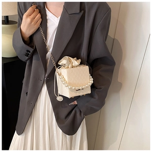 Detail of cream box bag featuring pearl handle, metal chain and textured finish