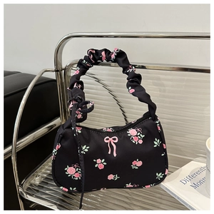 Detail van zwarte halvemaanvormige tas met rozenprint en een geplooid handvat