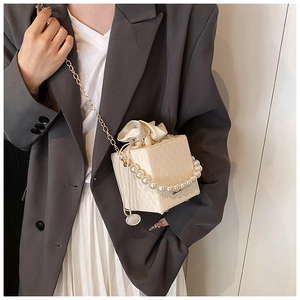 Close-up of cream square bucket bag with pearl handle and silk drawstring lining