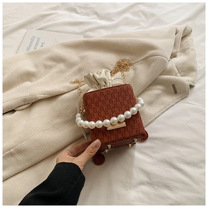 Detailed view of brown woven bucket bag with pearl handle and golden chain strap