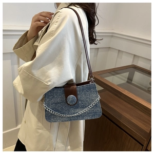 Détail du sac sous le bras en denim bleu avec chaîne argentée et rabat en cuir marron