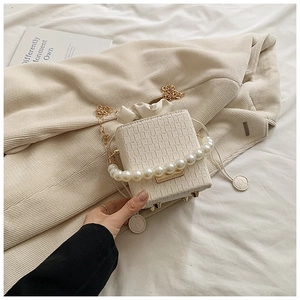 Detail of white corduroy bucket bag featuring pearl handle and gold chain strap