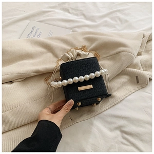 Detail of black woven bucket bag with pearl handle and golden chain on soft textile