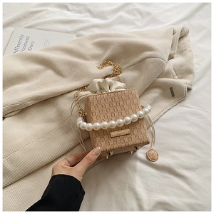 Detail of woven texture handbag with pearl handle, gold chain and protective base studs