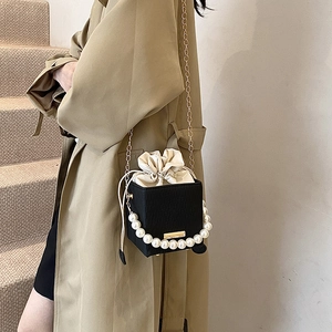 Black cubic crossbody bag with pearl handle and golden chain, minimalist bucket style