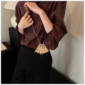 Detailed close-up of a golden shell-shaped mini bag with a fine chain strap on a model