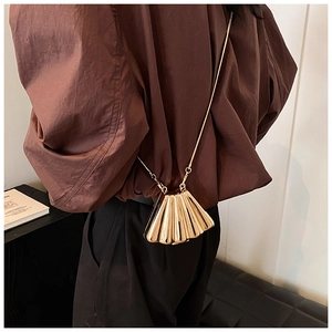 Close-up of golden metallic pleated shell bag with polished finish and chain strap