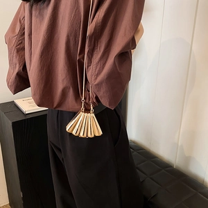 Elegant gold shell-shaped clutch bag with fine chain strap held by a model