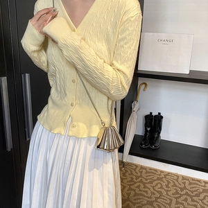 Pale yellow cable-knit cardigan with V-neck and a metallic shell-shaped crossbody bag