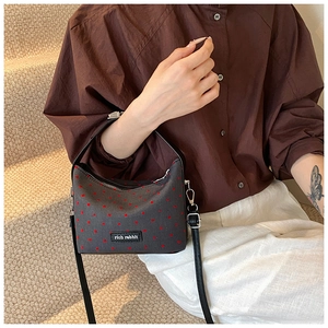 Détail d'un mini sac gris à motifs coeurs rouges porté par un mannequin sur l'escalier