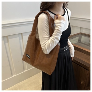 Detail of a brown leather tote bag with a black FASHION tag worn by a model in an office