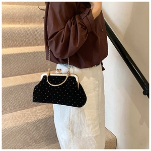 Close-up of a black velvet kiss-lock bag with white polka dots and gold chain strap