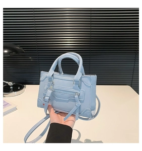 Close-up of light blue trapezoid handbag with tassel zippers and metal buckles