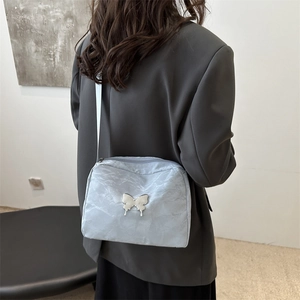 Light blue nylon crossbody bag with silver butterfly charm on modern female model