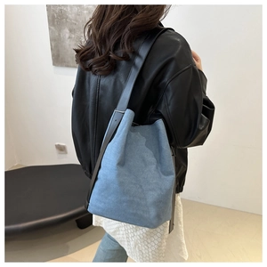 Détail du sac seau en denim bleu clair avec bandoulière en cuir noir et boucle en métal