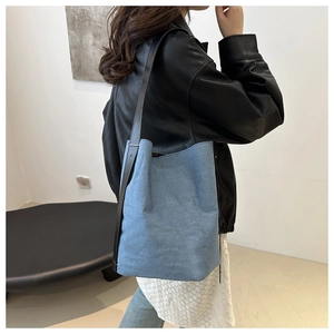 Détail du sac seau en denim bleu clair avec bandoulière en cuir noir sur un modèle