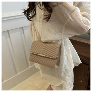 Detail of light beige V-quilted faux leather shoulder bag with golden chain strap
