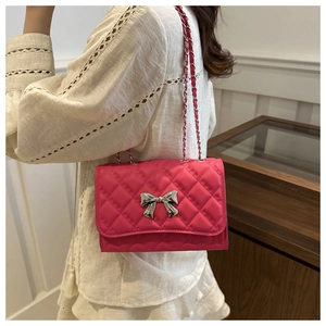 Detailed view of rose red quilted chain bag with silver bow clasp worn by a model