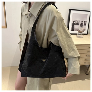 Close-up of black textured large tote bag with triangle logo worn with beige coat