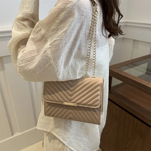 Minimalist beige crossbody bag with V-shaped quilting and gold chain strap on model