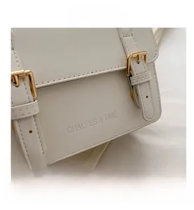 Detailed close-up of stitching and gold buckle straps on a white leather crossbody bag