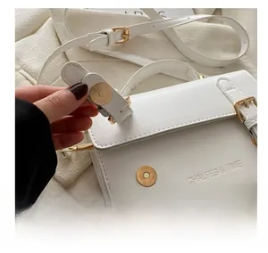 Detail of golden magnetic clasp and textured beige leather on a crossbody square bag