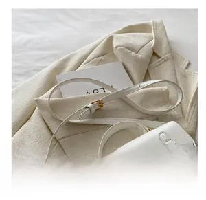 White leather crossbody bag detail with golden metal buckle on a beige tweed background