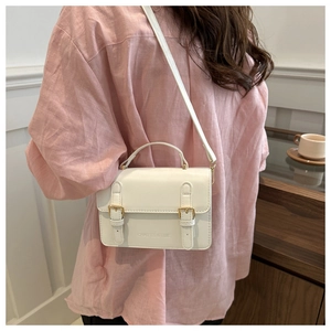 Close-up of elegant white rectangular crossbody bag with dual gold buckles and handle