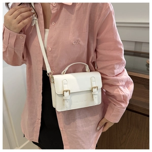 Close-up of white leather crossbody bag with golden buckles and metal branding details