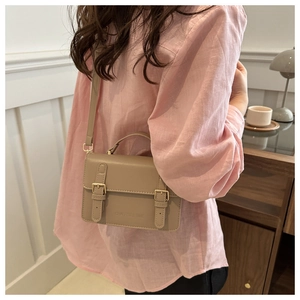 Detail view of khaki leather crossbody bag with dual gold buckle straps and top handle