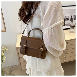 Detail of vintage brown crossbody bag with gold buckles and embossed texture on flap