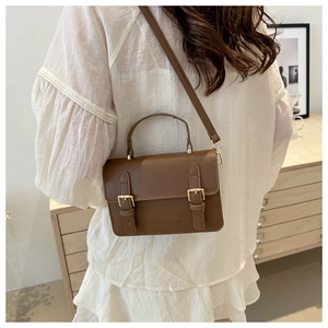 Brown faux leather crossbody bag with flap dual buckles shown in a lifestyle home setting