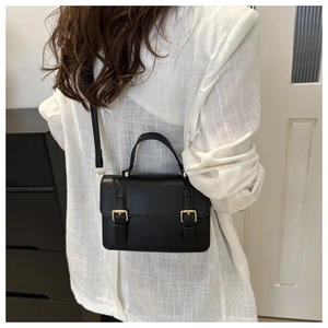 Detail of a black mini crossbody bag with gold buckles worn by a model in white linen