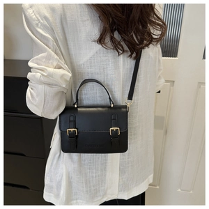 Detail of black leather crossbody bag with dual golden buckles shown on model