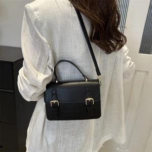 Classic black leather crossbody bag with dual belt buckles worn by a model in a minimal room